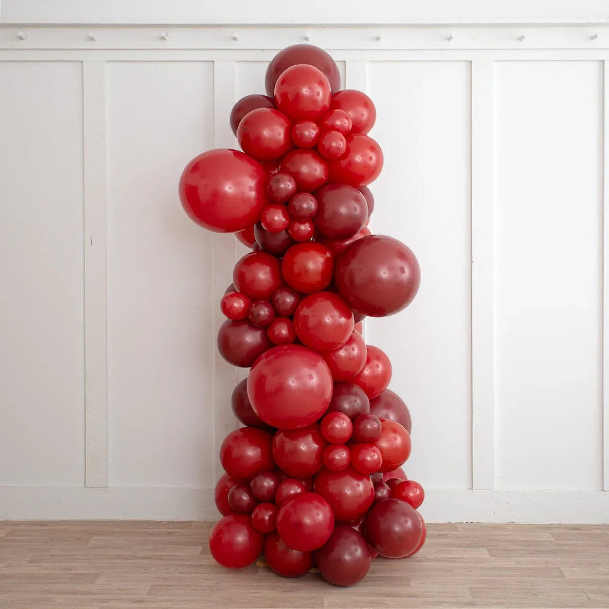 Dark cherry red inflated balloon pillar decoration against white paneled wall on wooden floor
