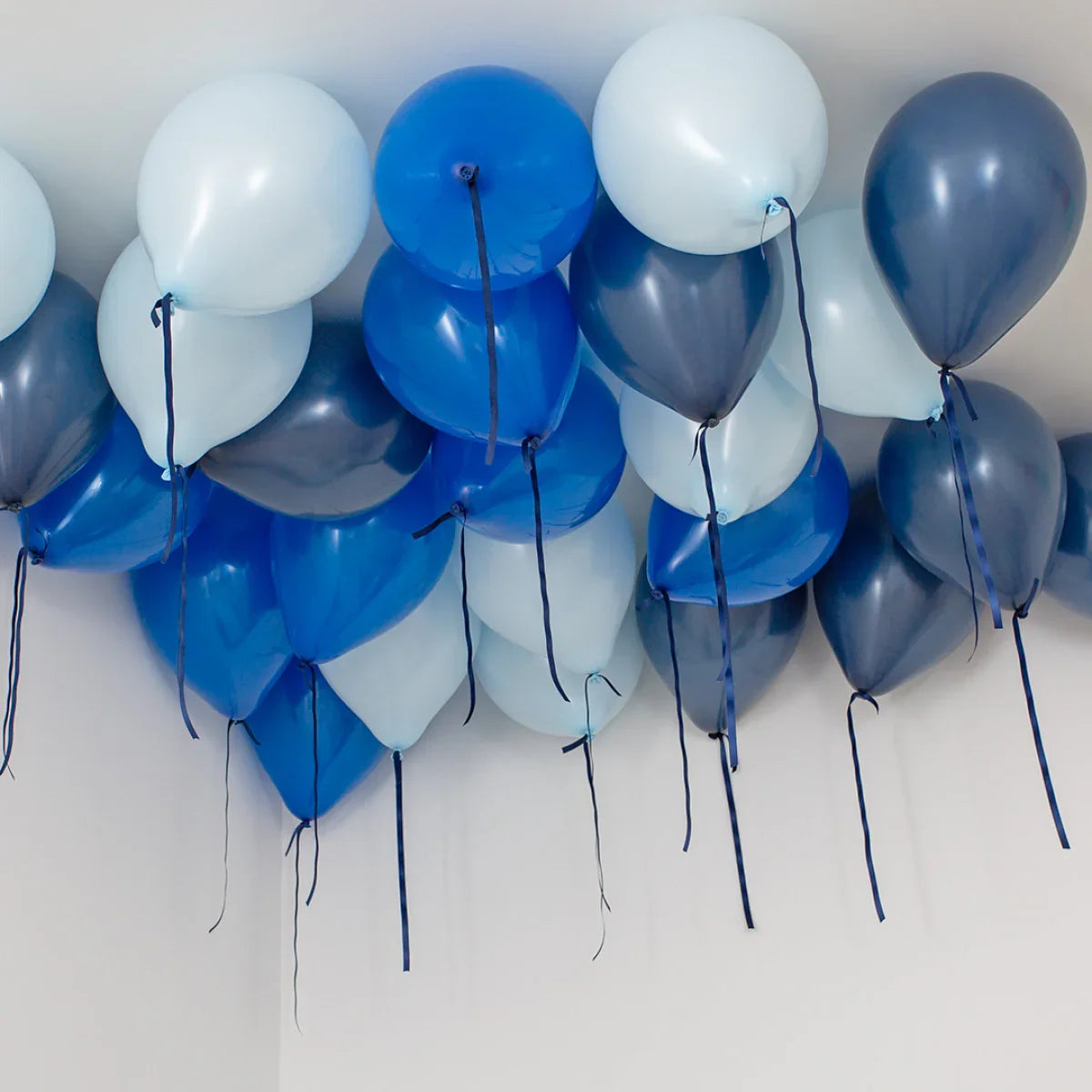 Deep blue, navy, and white helium balloons floating on a ceiling with ribbons