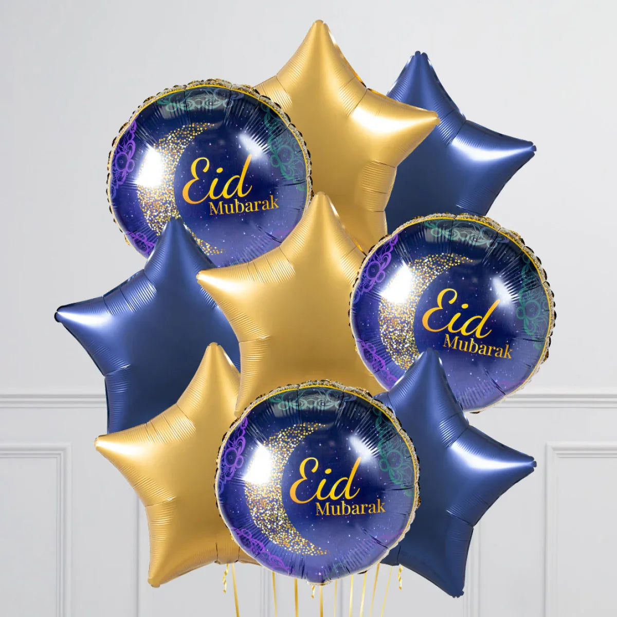 Eid Mubarak stars and moon foil balloons in gold and blue against a white wall