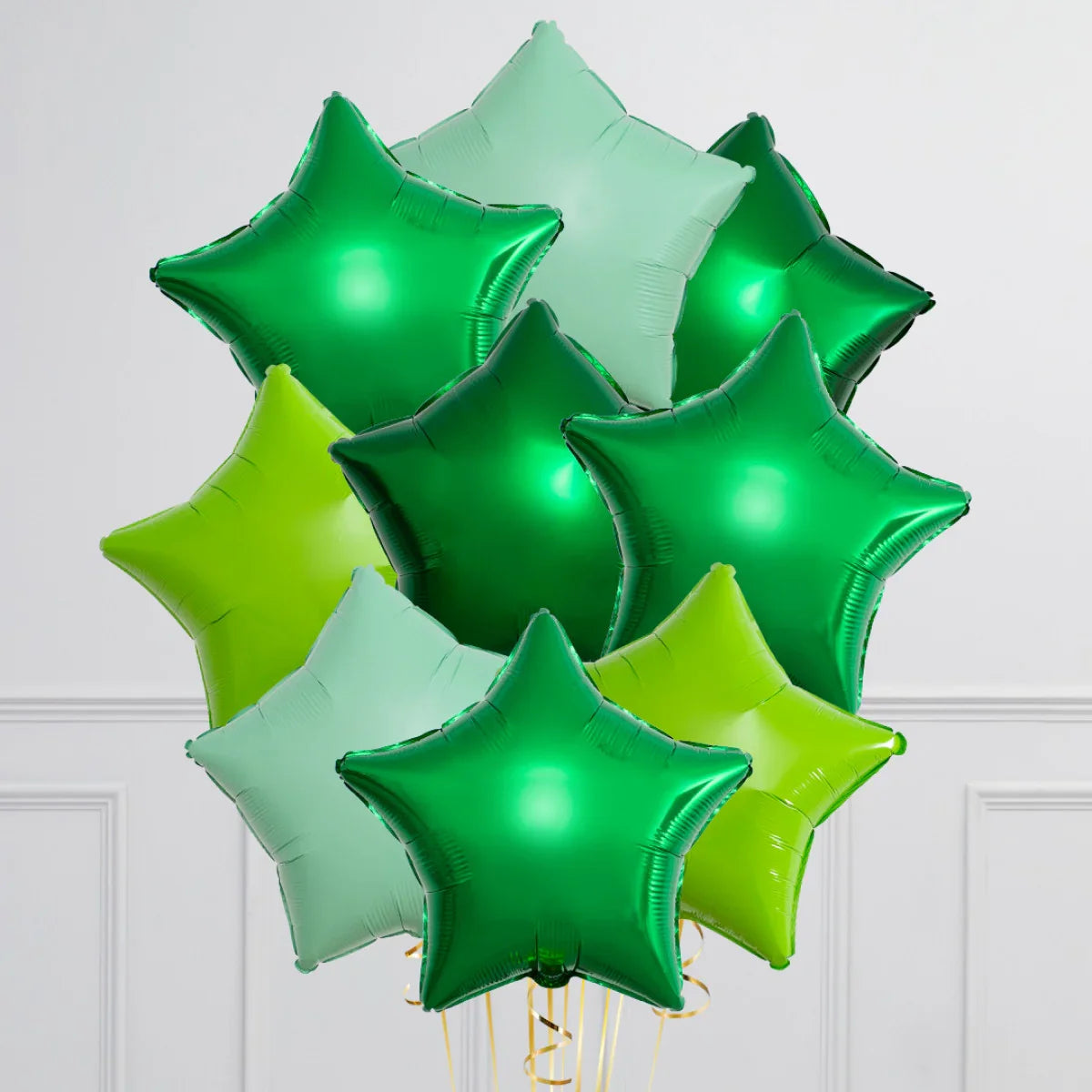 Bunch of star-shaped foil balloons in various shades of green against white paneled wall