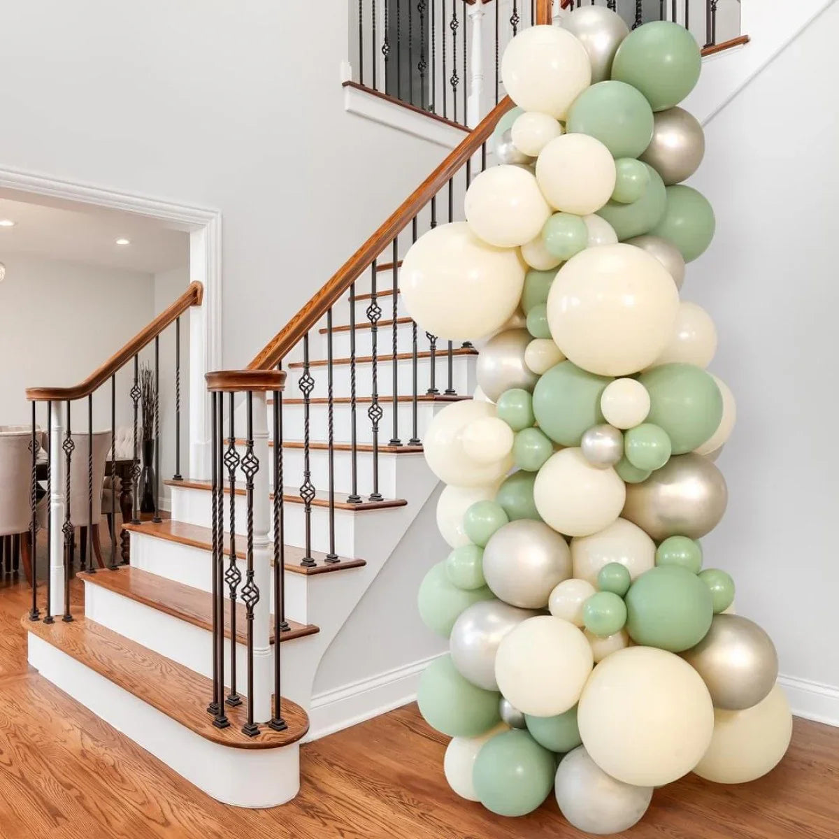Eucalyptus-themed balloon pillar in green, cream, and metallic silver at wooden staircase interior
