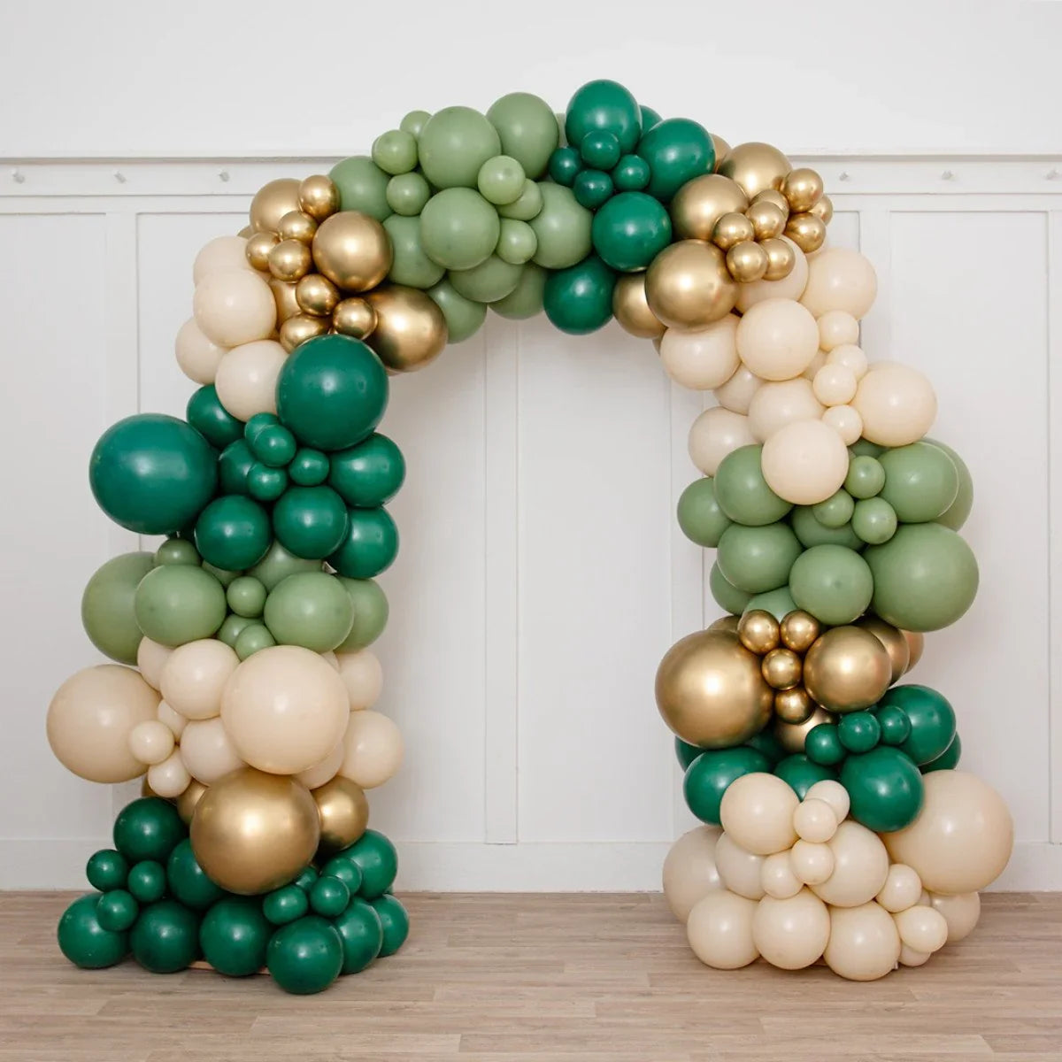 Ready-made balloon arch with green, cream, and gold balloons on wood floor and white wall backdrop