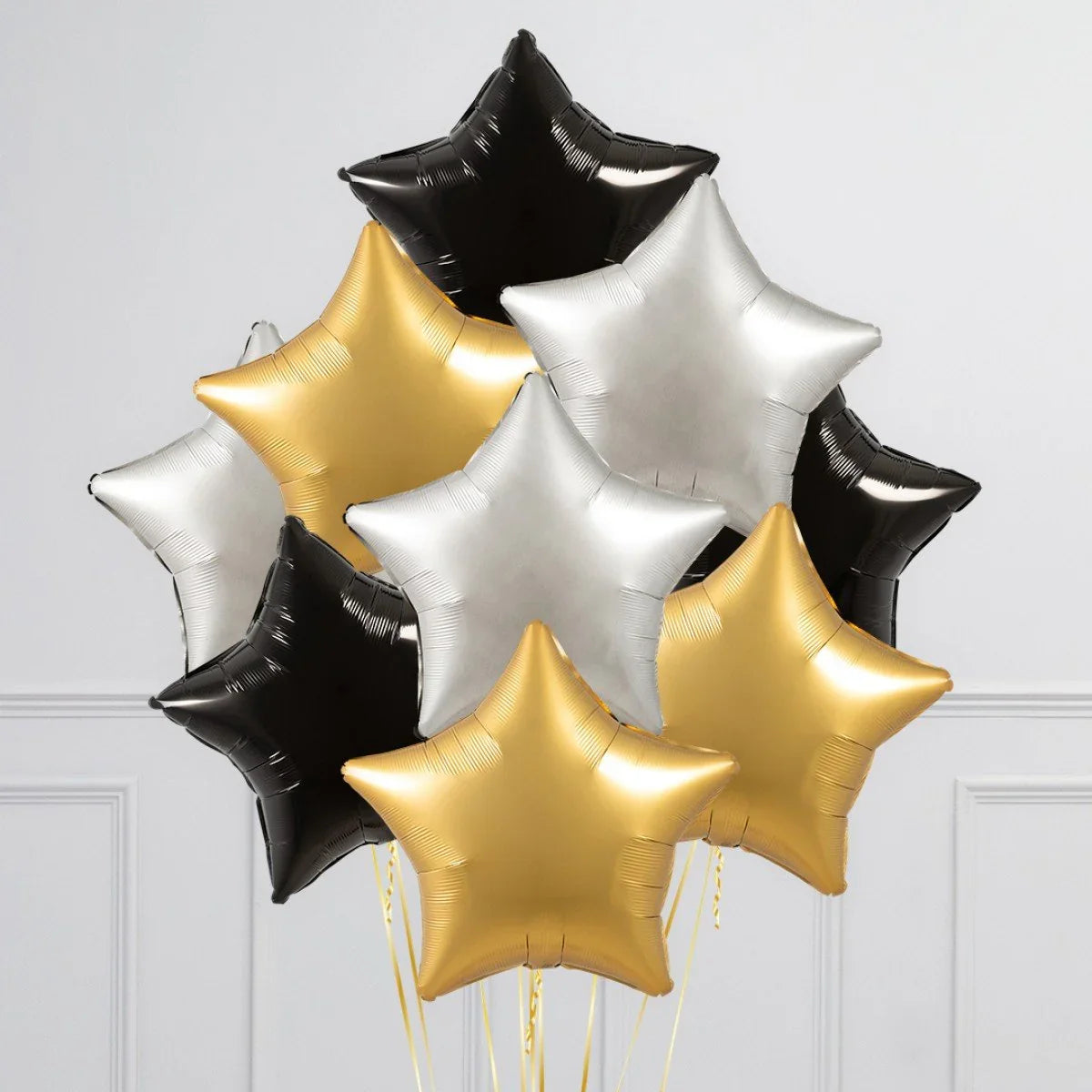 Cluster of black, gold, and silver star-shaped foil balloons against a white panel wall