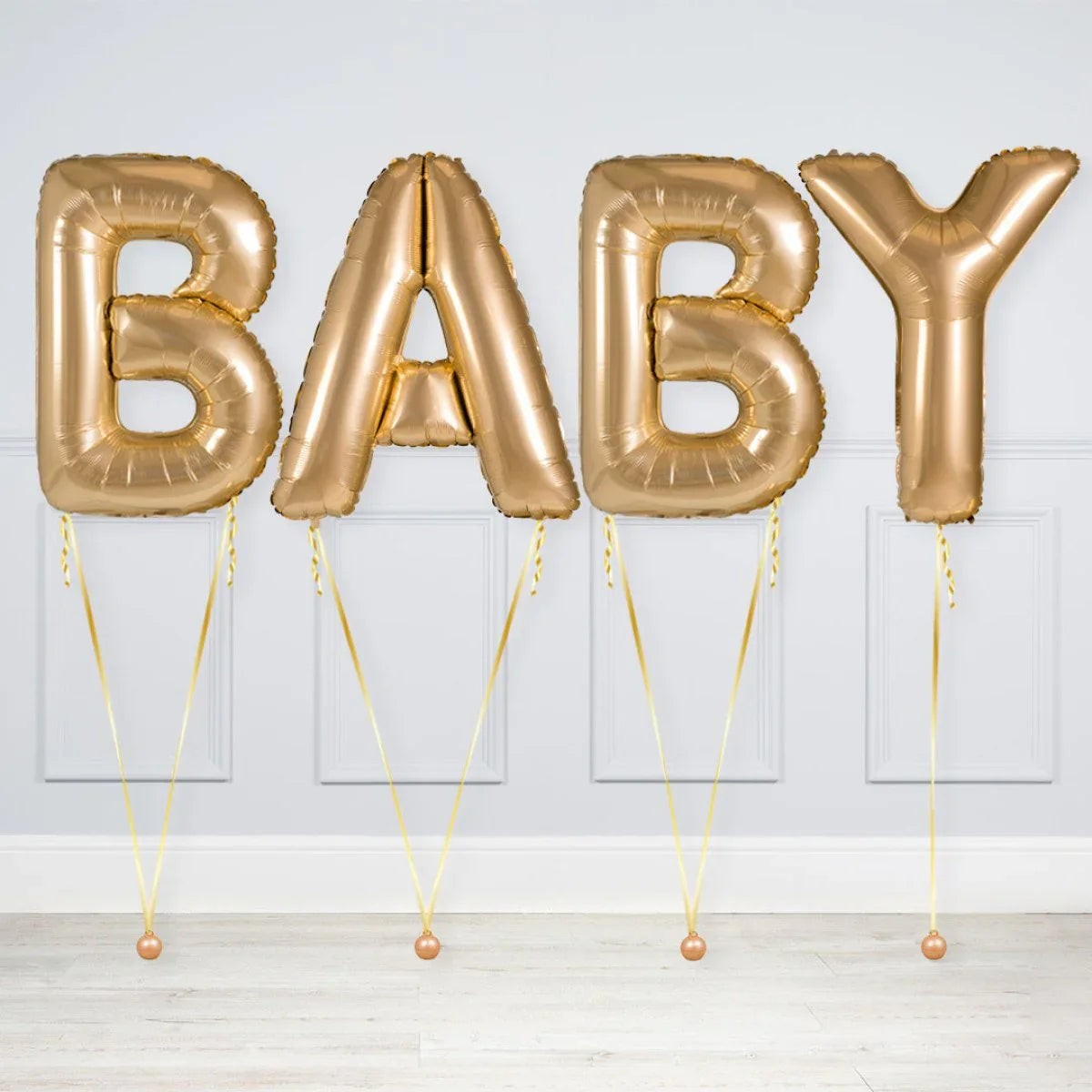 Gold foil balloons spelling BABY against a white paneled wall, party decoration