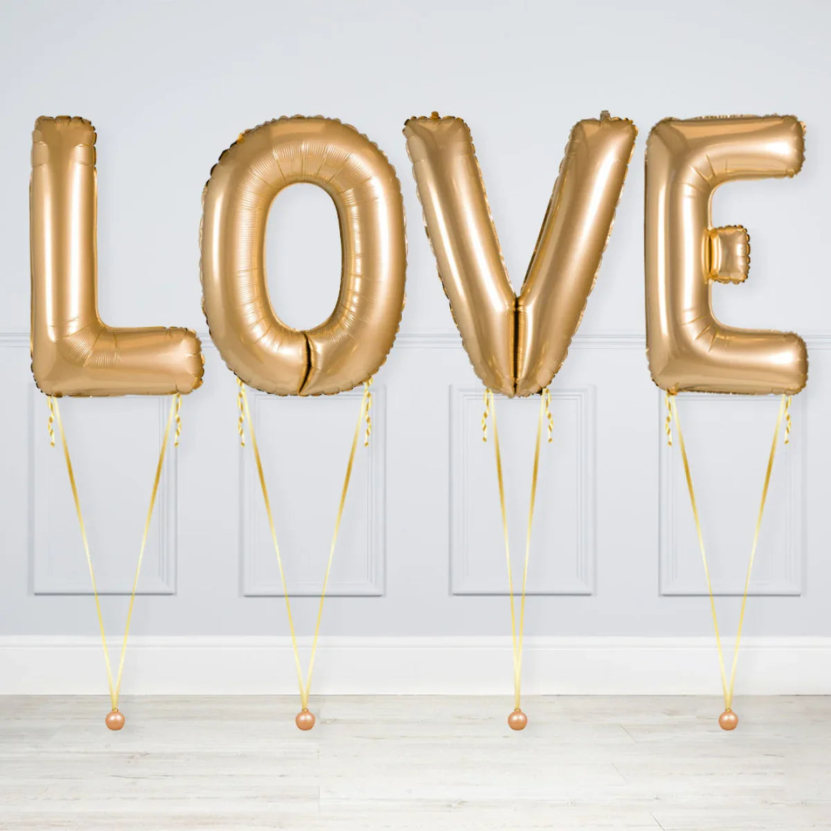 Gold foil balloons spelling LOVE with ribbon weights in a white room with panel walls