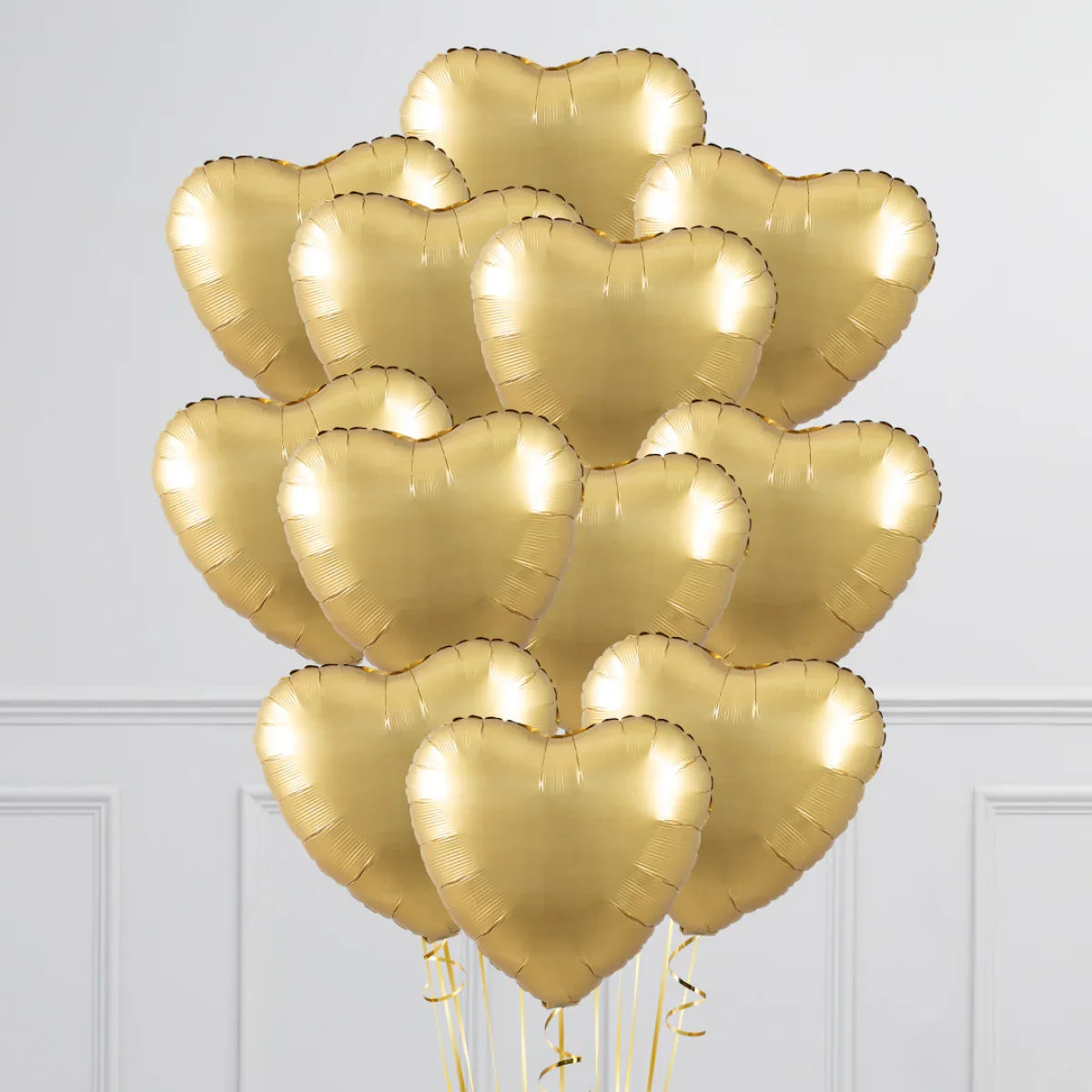 Bunch of shiny gold heart-shaped foil balloons indoors with white paneled wall background