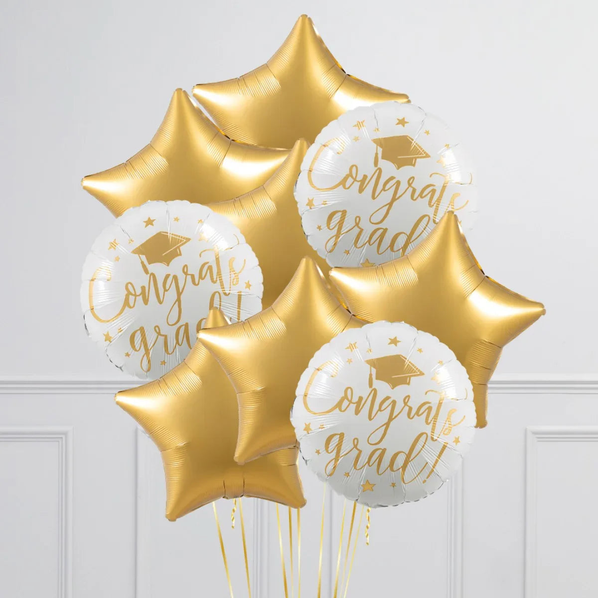Gold star and white Congrats Grad foil balloons with graduation cap design indoors