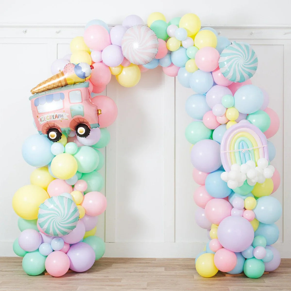 Pastel balloon arch with ice cream truck and rainbow foil balloons on wooden floor