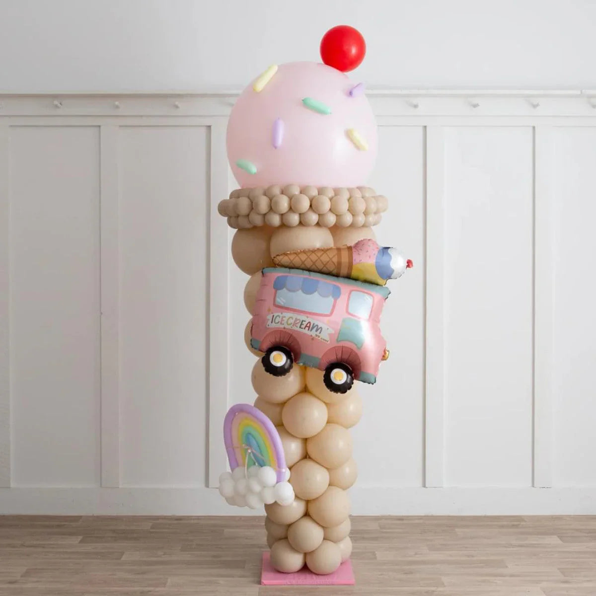 Ice cream cone balloon pillar with pastel balloons, ice cream truck, and rainbow shapes on wooden floor