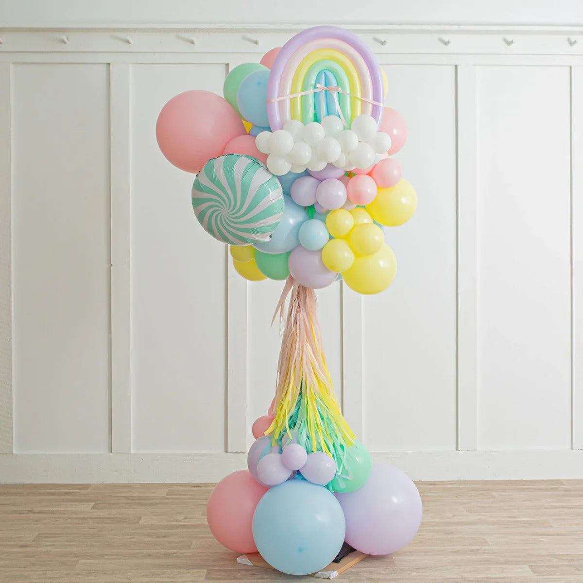 Colorful pastel balloon bouquet with rainbow and cloud shapes against white wall