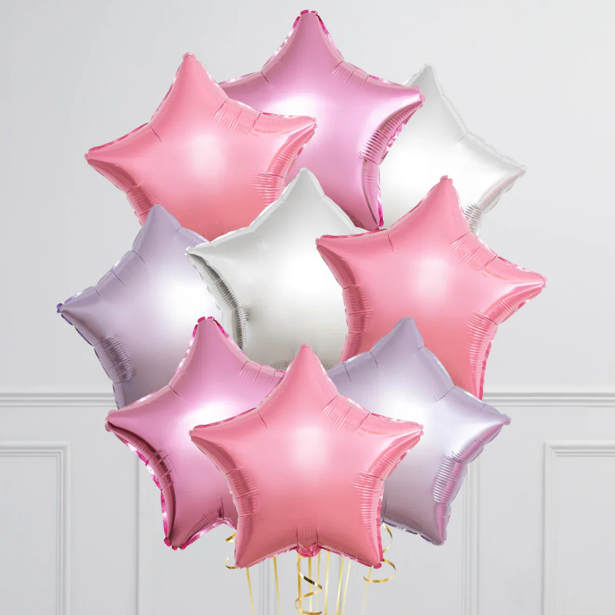 Cluster of pink, silver, and light purple star-shaped foil balloons against white wall