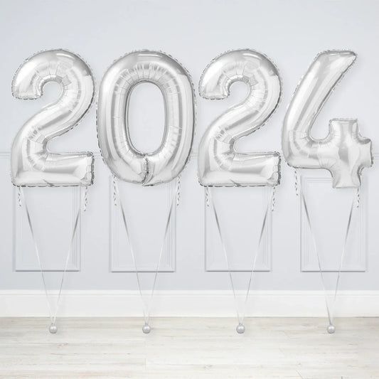 Silver metallic foil balloons shaped as numbers forming 2024 against white wall, party decoration