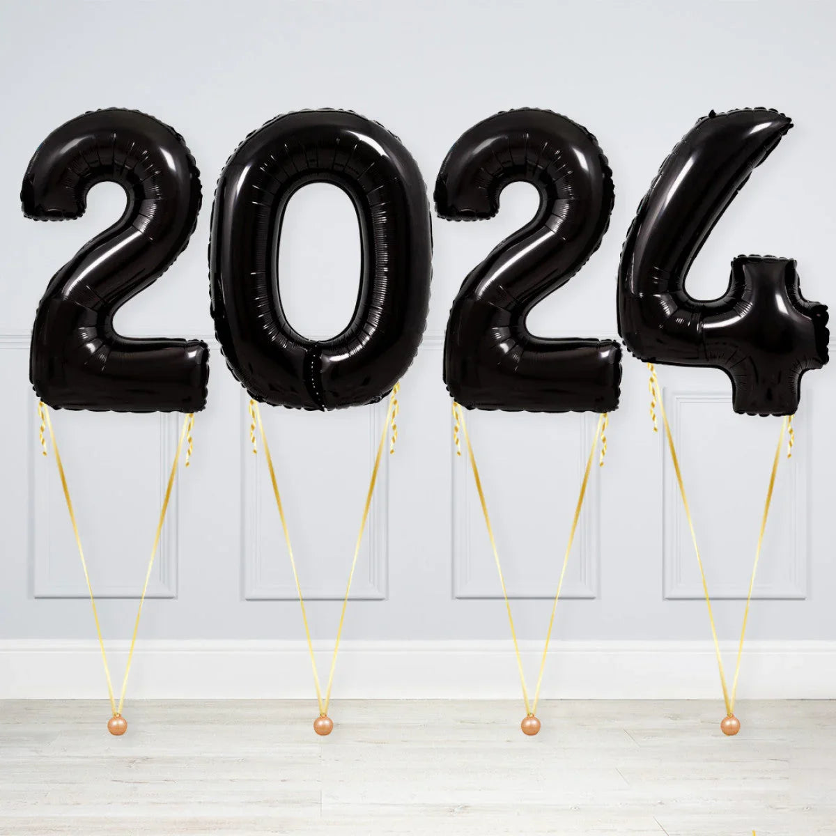 Black inflatable number balloons forming 2024 with gold ribbons against gray wall