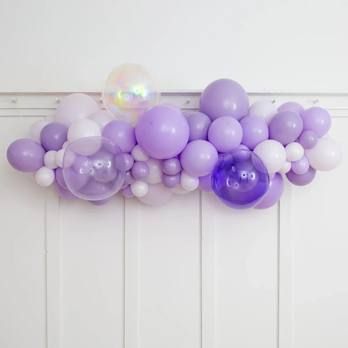 Lavender balloon garland with white and transparent balloons hung on white paneled wall