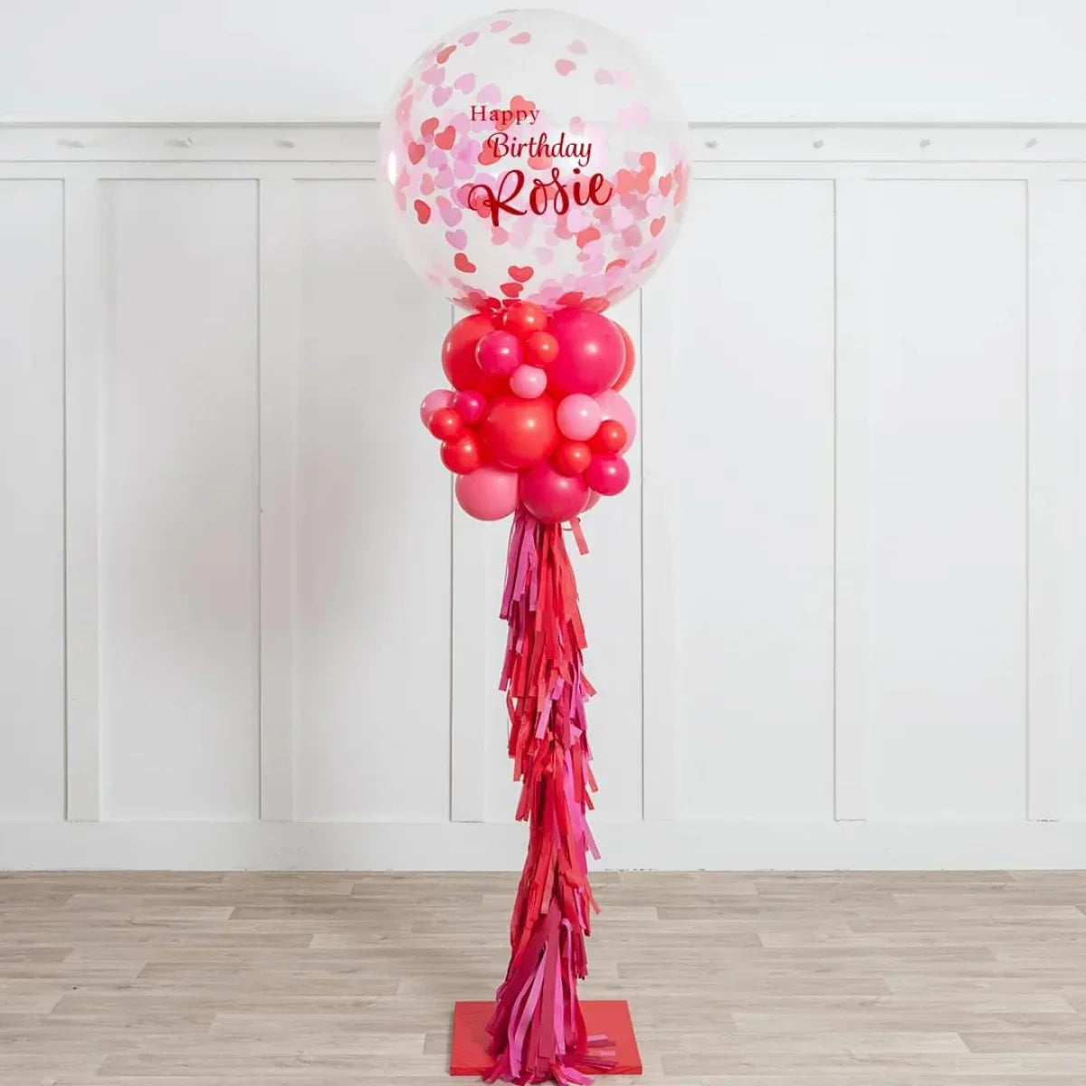 Birthday balloon pillar with red and pink balloons and heart confetti in clear balloon
