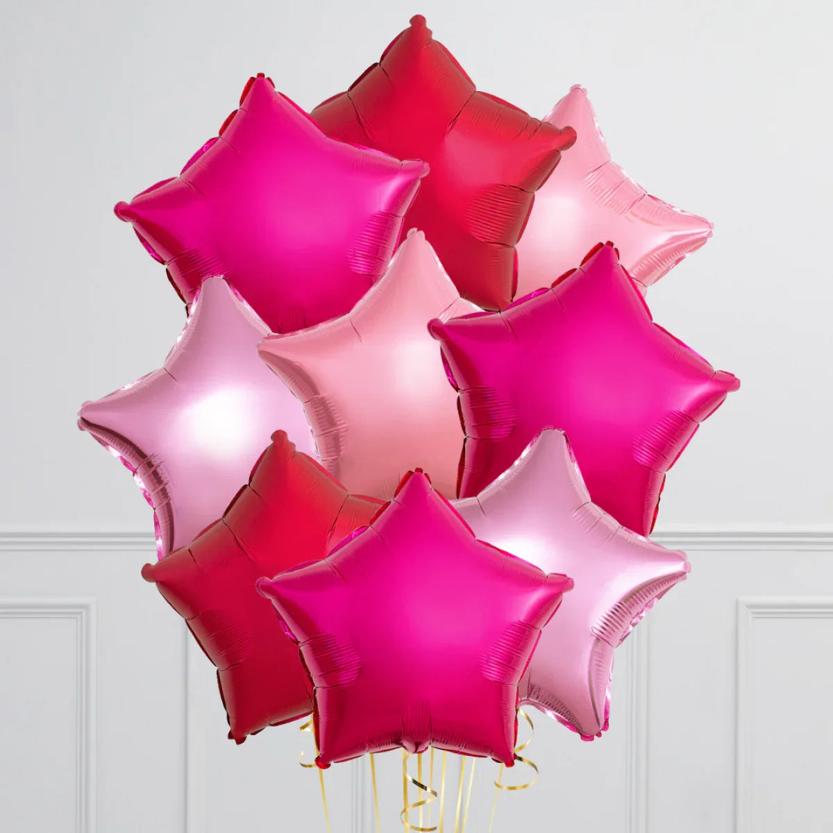 Bunch of shiny red, pink, and magenta star-shaped foil balloons with gold ribbons indoors