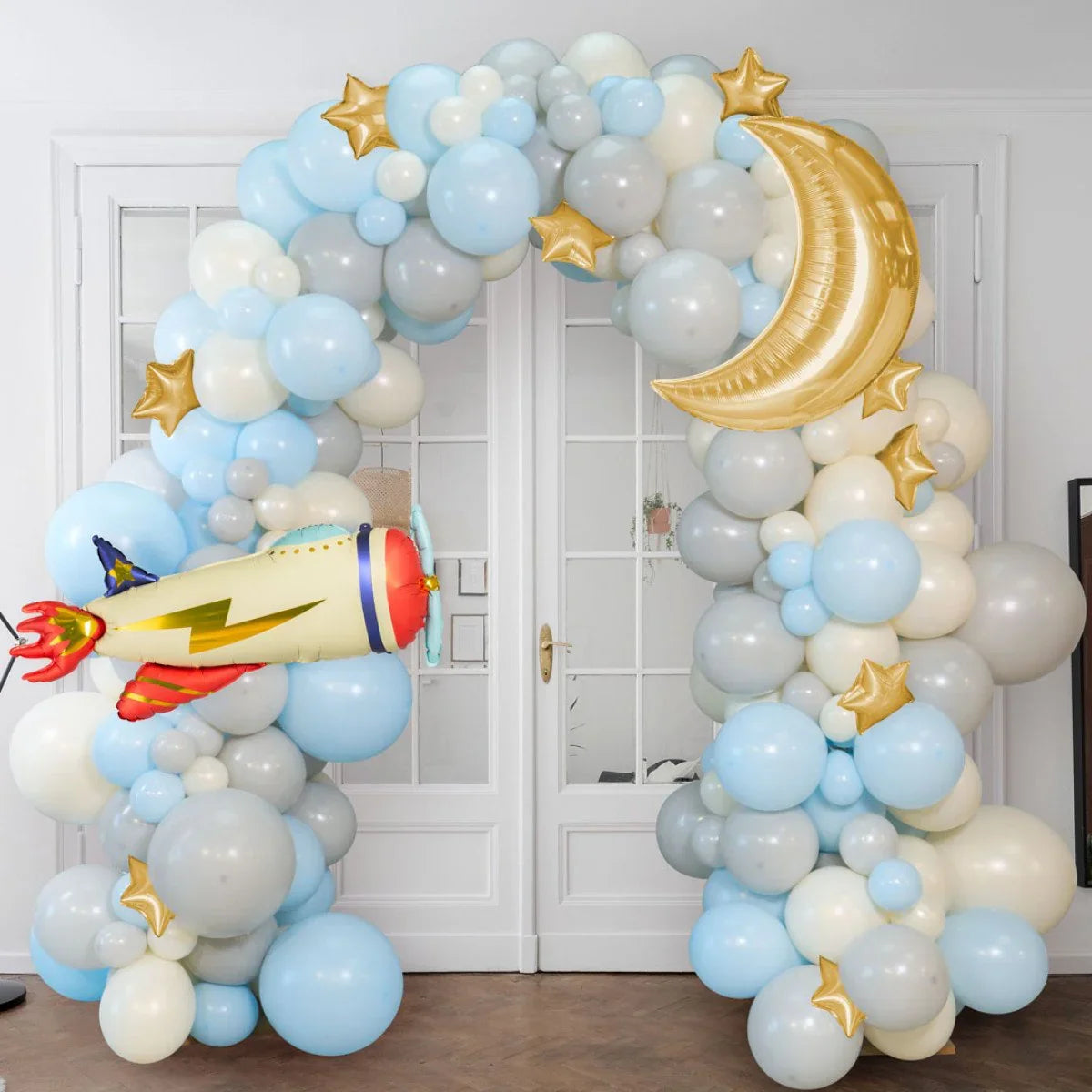 Blue, white, and gray balloon arch with gold stars, crescent moon, and rocket foil balloons indoors