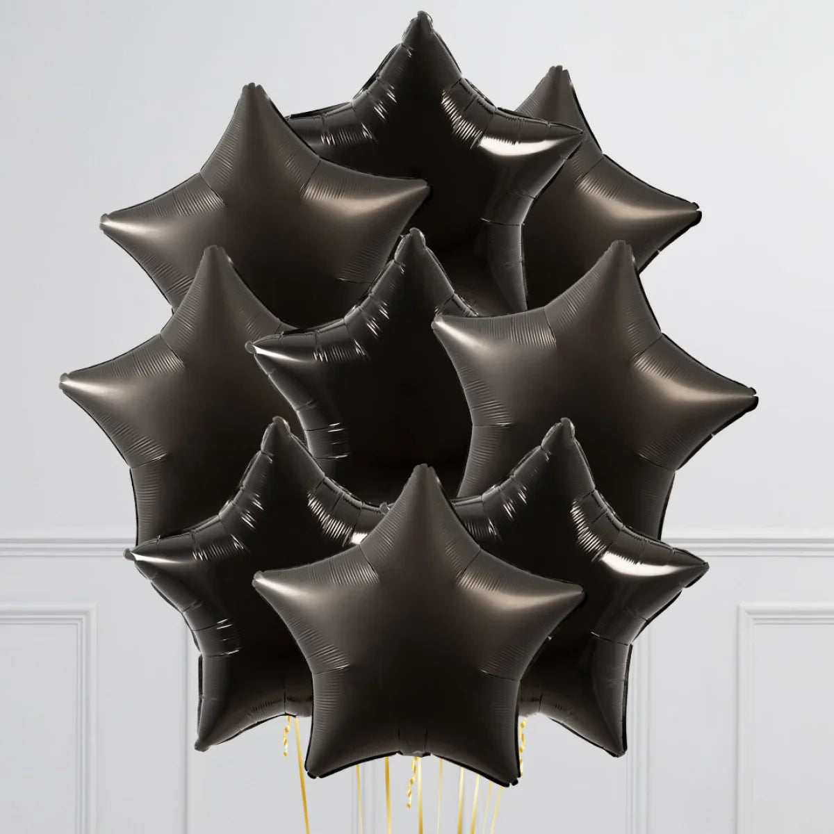 Cluster of shiny black star-shaped foil balloons with yellow ribbons against a white wall