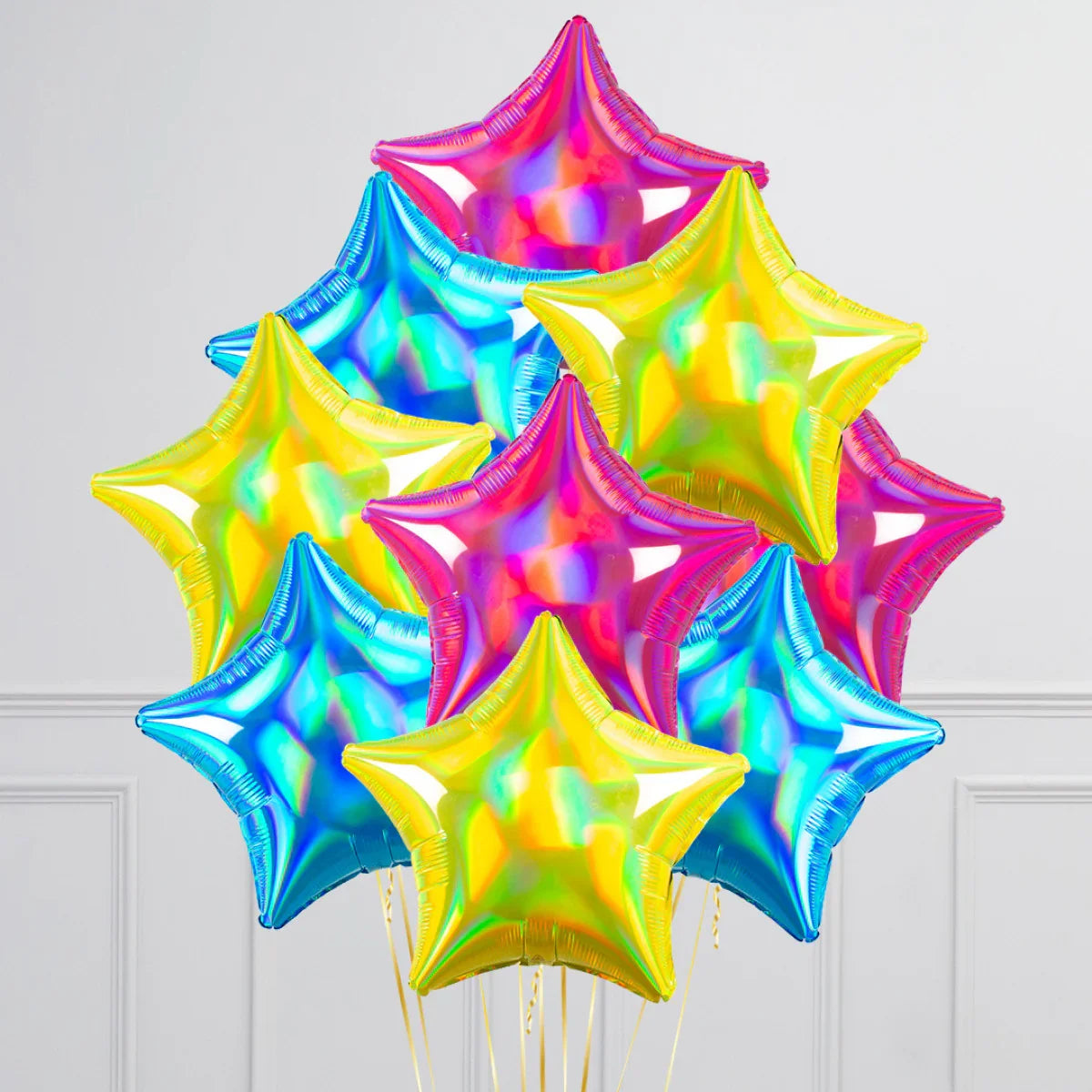 Bunch of shiny star-shaped foil balloons in pink, blue, and yellow colors against white wall