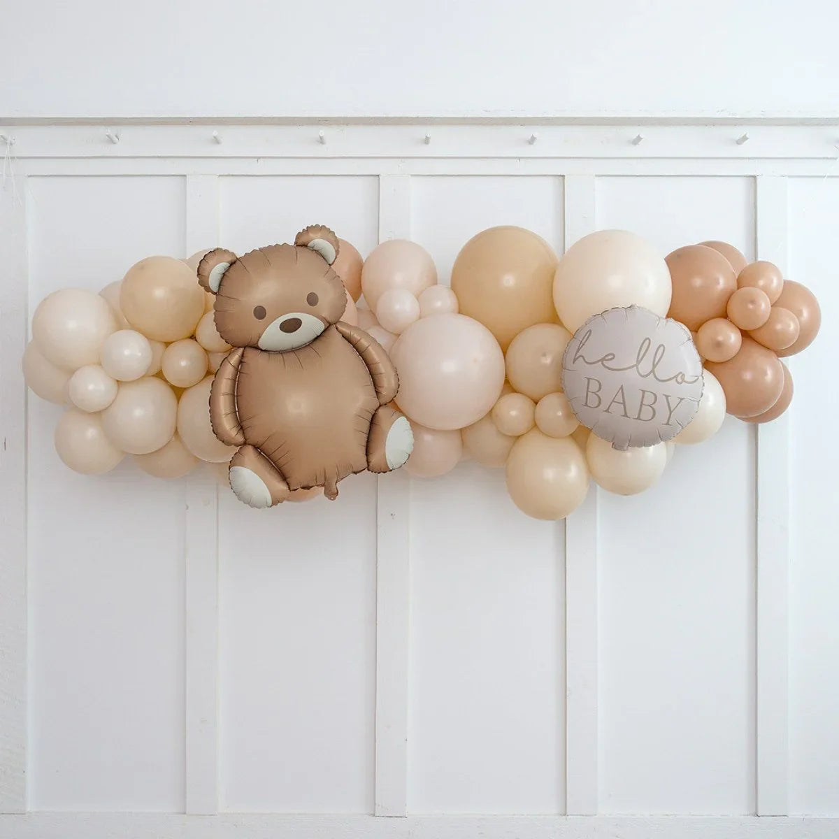 Neutral beige balloon garland with teddy bear and hello baby balloon on white wall backdrop