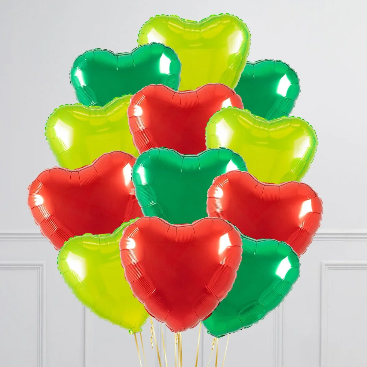 Bright red, green, and yellow heart-shaped foil balloons clustered indoors against a white wall
