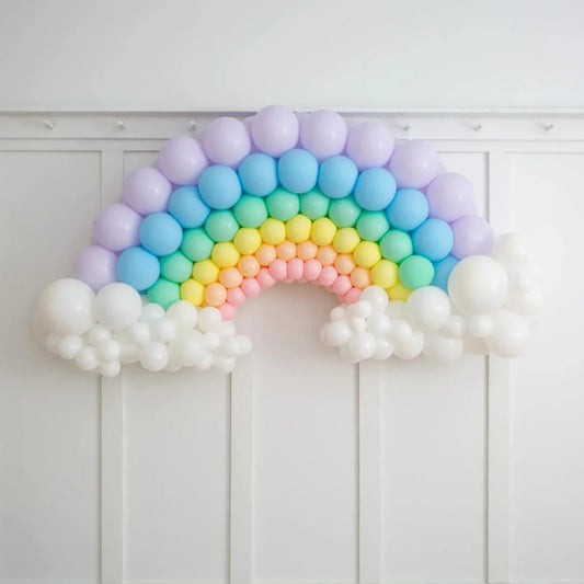 Pastel rainbow balloon arch with white cloud-shaped balloons on white paneled wall