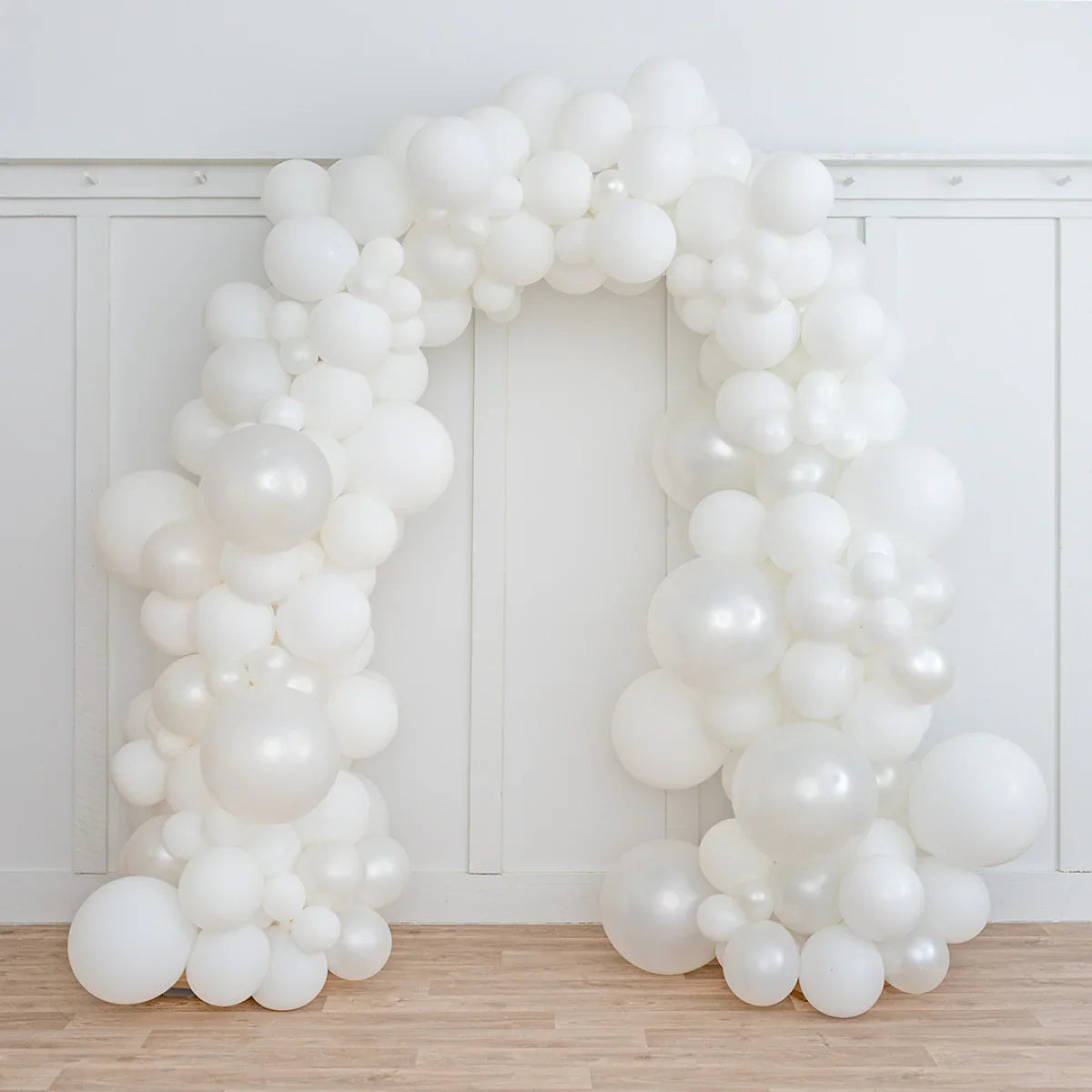 Elegant pearl white balloon arch against white paneled wall on wooden floor