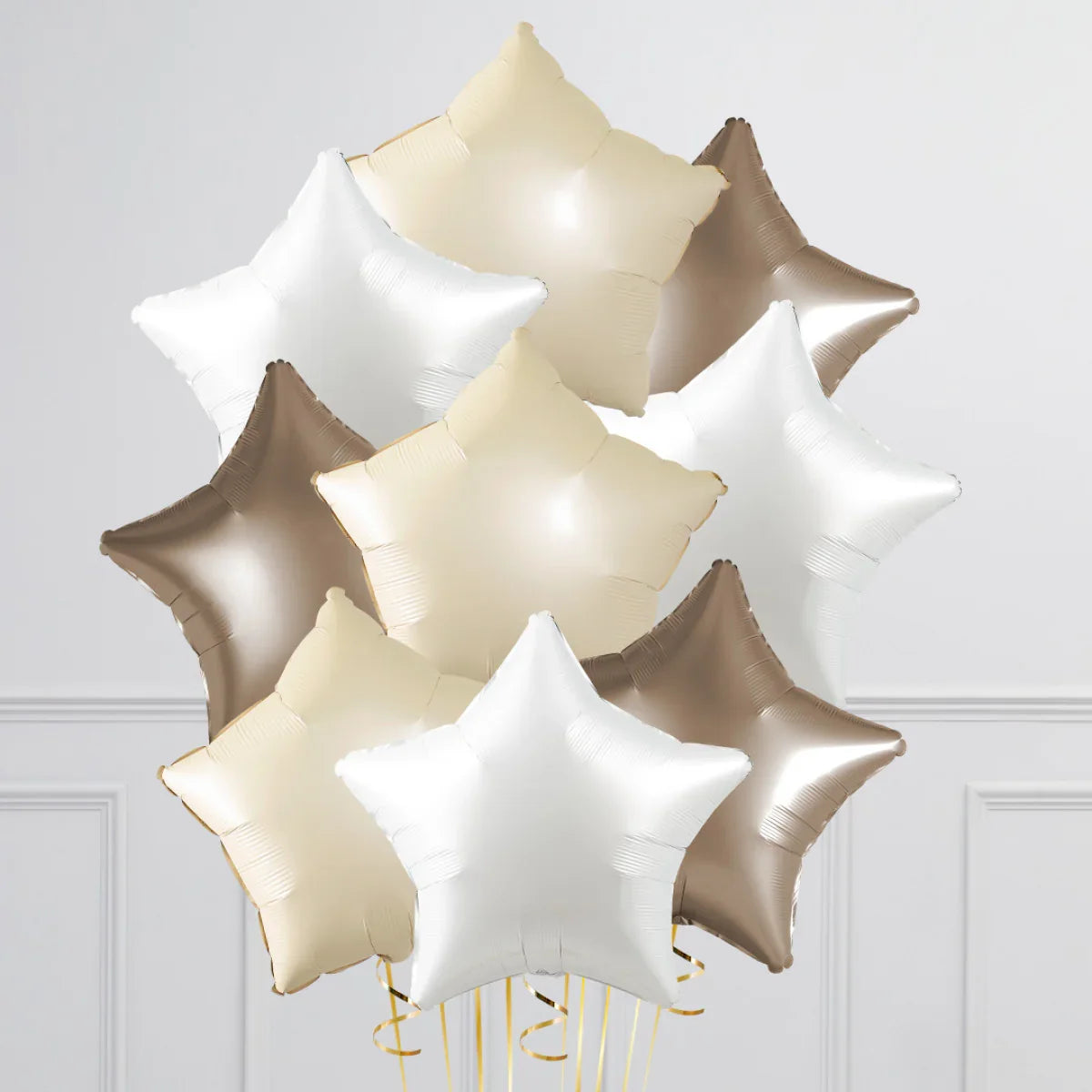 Bunch of pearl sand, white, and brown star-shaped foil balloons against a white wall