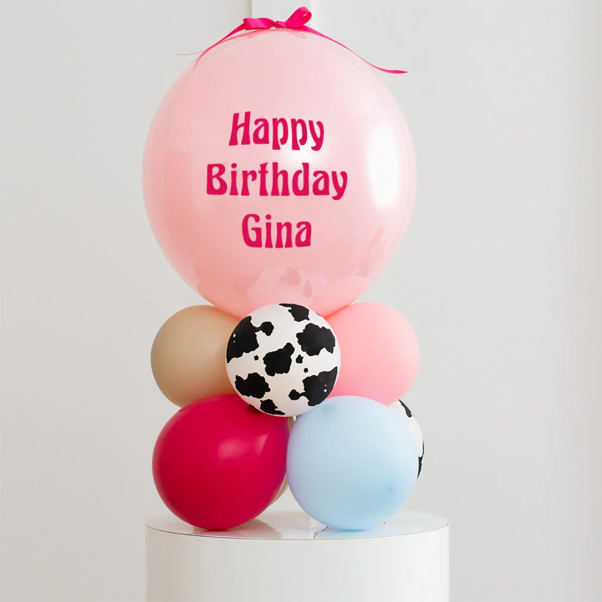 Personalised pink birthday balloon with message Happy Birthday Gina on bubble balloon stack with multi-colored and cow print balloons