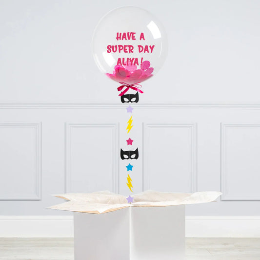 Personalised bubble balloon with pink confetti, superhero decorations, and gift box