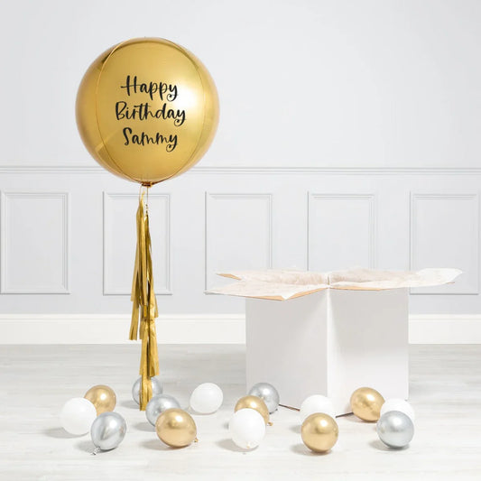 Personalised gold birthday balloon with tassels, box, and metallic balloons in modern room
