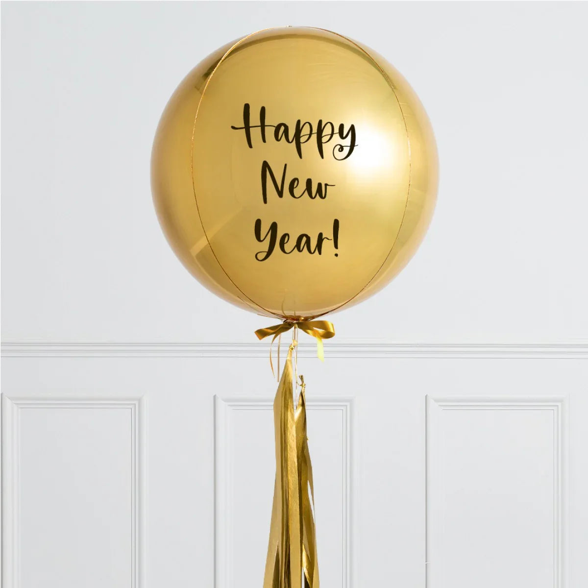 Large gold foil balloon with "Happy New Year!" text and gold tassel hanging in a white interior