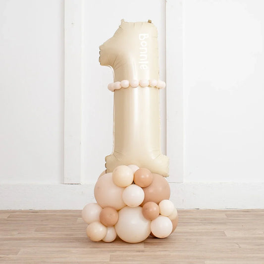 Beige number one balloon with smaller neutral balloons base on wooden floor against white wall