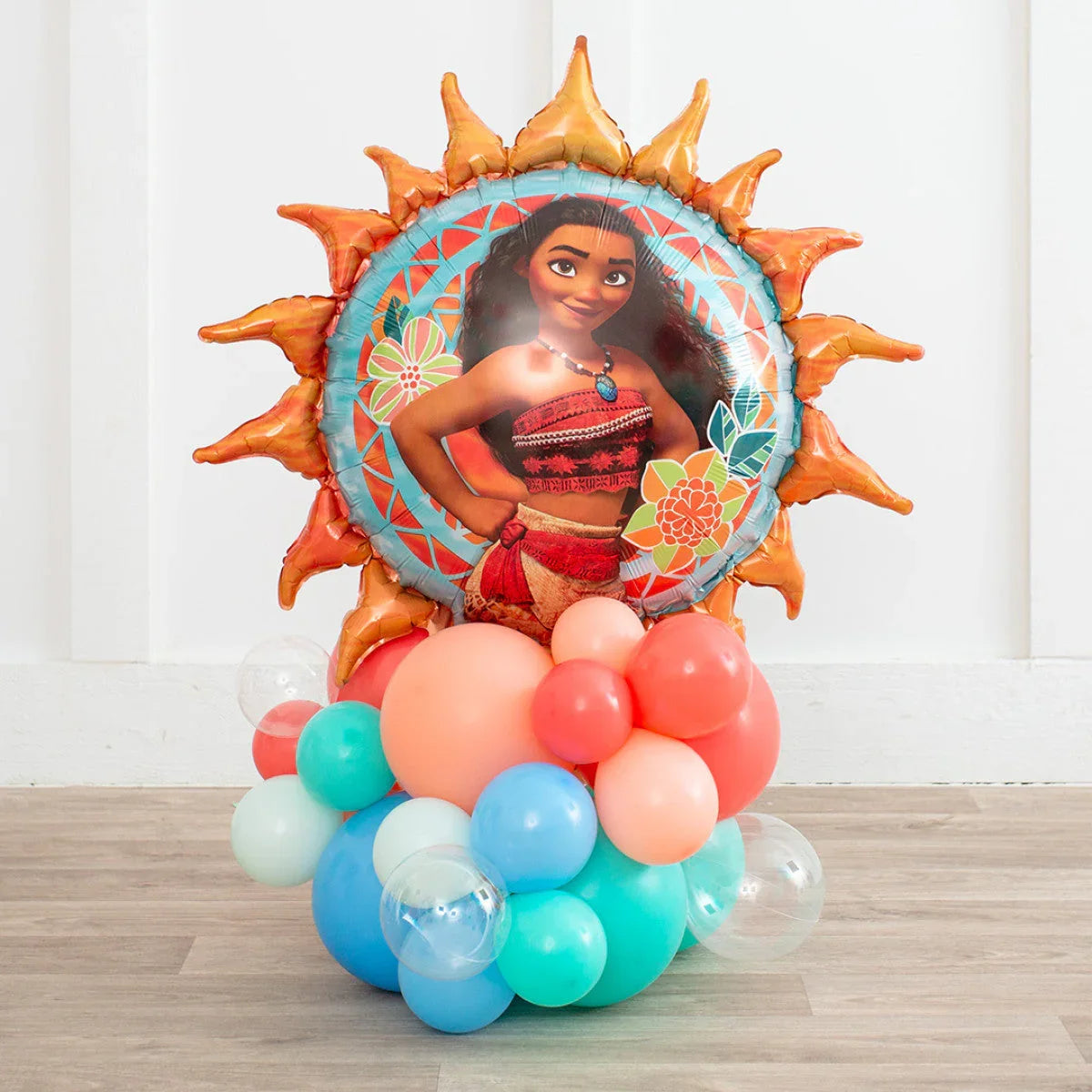 Moana-themed sun foil balloon with assorted coral, blue, and clear balloons on wood floor
