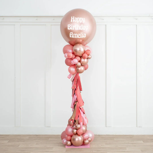 Rose gold and blush pink personalized birthday balloon pillar with Happy Birthday Amelia text