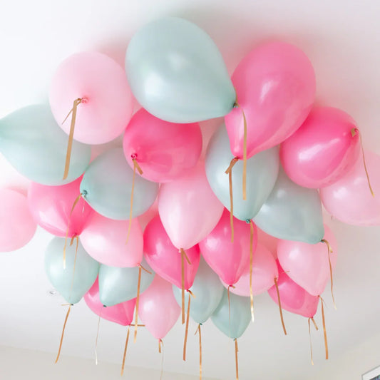 Helium-filled pink and mint balloons clustered on a white ceiling with gold ribbons