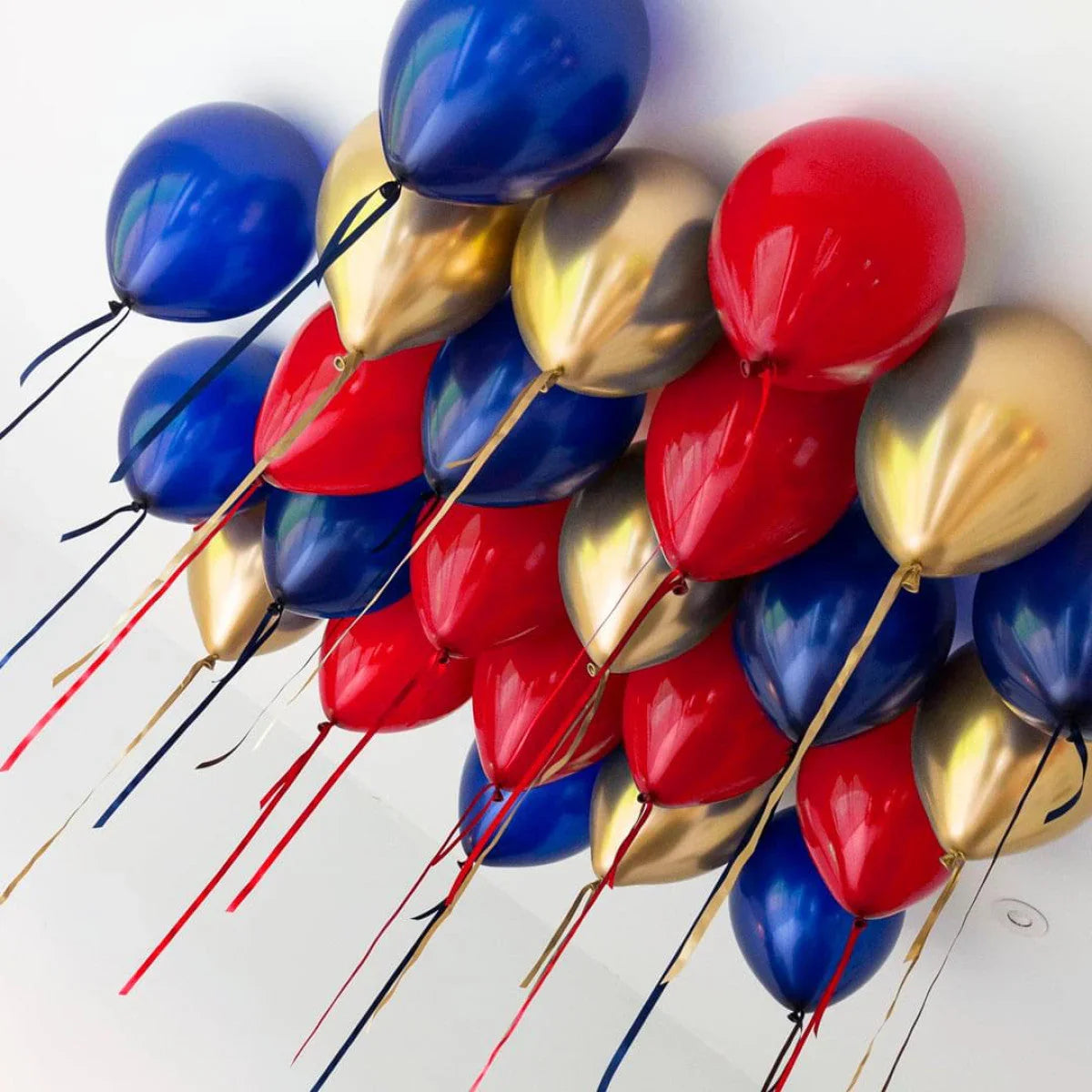 Cluster of red, blue, and gold helium balloons floating on white ceiling with hanging ribbons