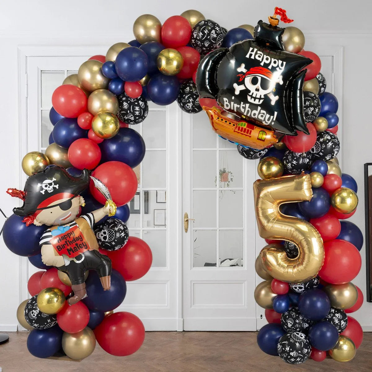 Pirate-themed balloon arch with red, blue, gold, and skull-patterned balloons, pirate ship and number 5