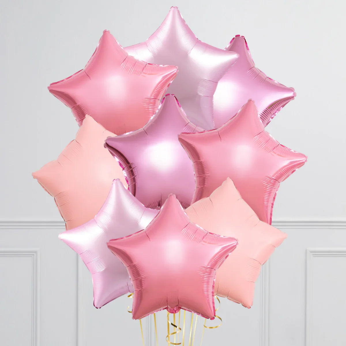bunch of shiny pink and purple star-shaped foil balloons indoors with white paneled wall background