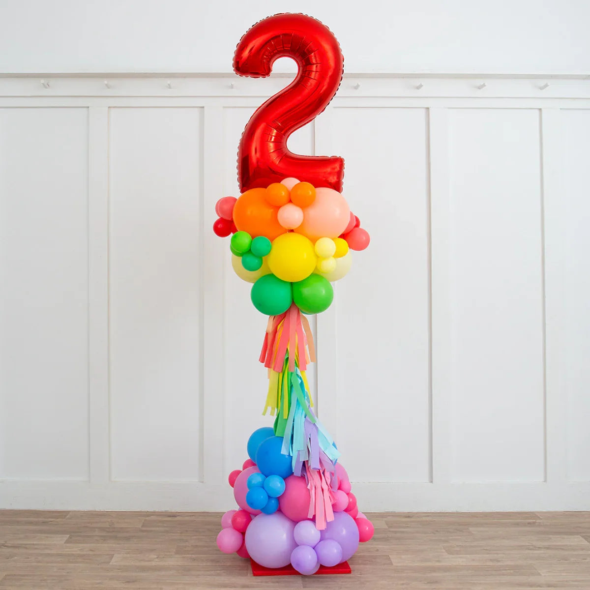 Colorful balloon pillar with large red number 2 balloon and rainbow fringe in a white room