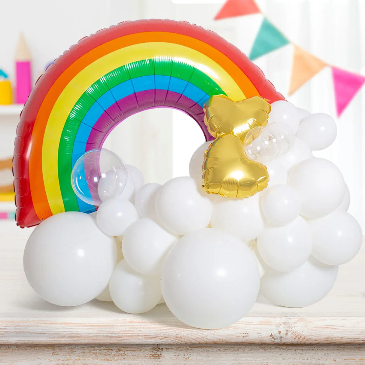 Colorful rainbow foil balloon arch with white balloons and gold heart-shaped balloons on wooden table