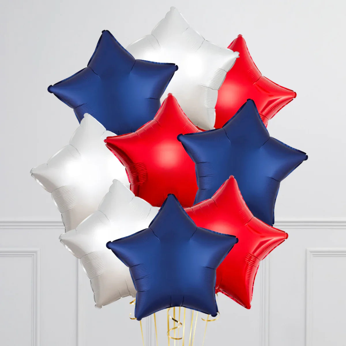 Cluster of red, white, and blue star-shaped foil balloons against a white wall background