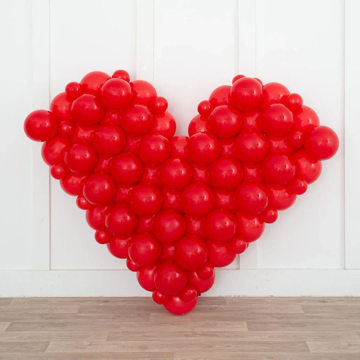 Large red heart shape made of clustered round balloons against white paneled wall and wooden floor