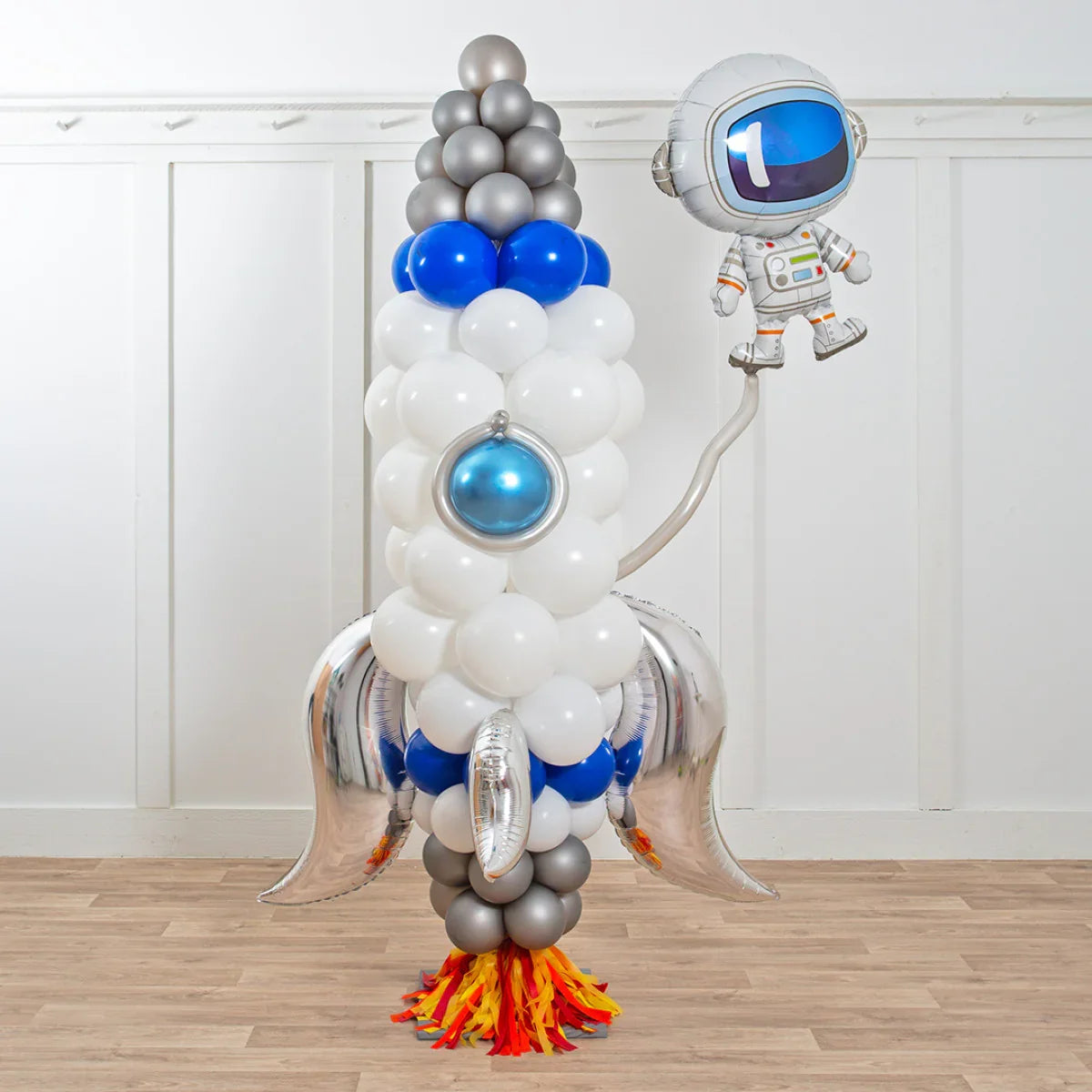 Deluxe balloon sculpture of a rocket with silver fins, flame base, and an astronaut balloon in white room