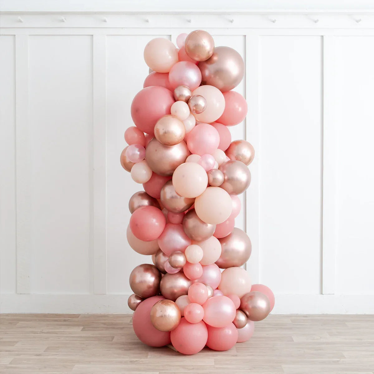 Rose gold and blush pink balloon pillar decoration indoors on wooden floor and white paneled wall