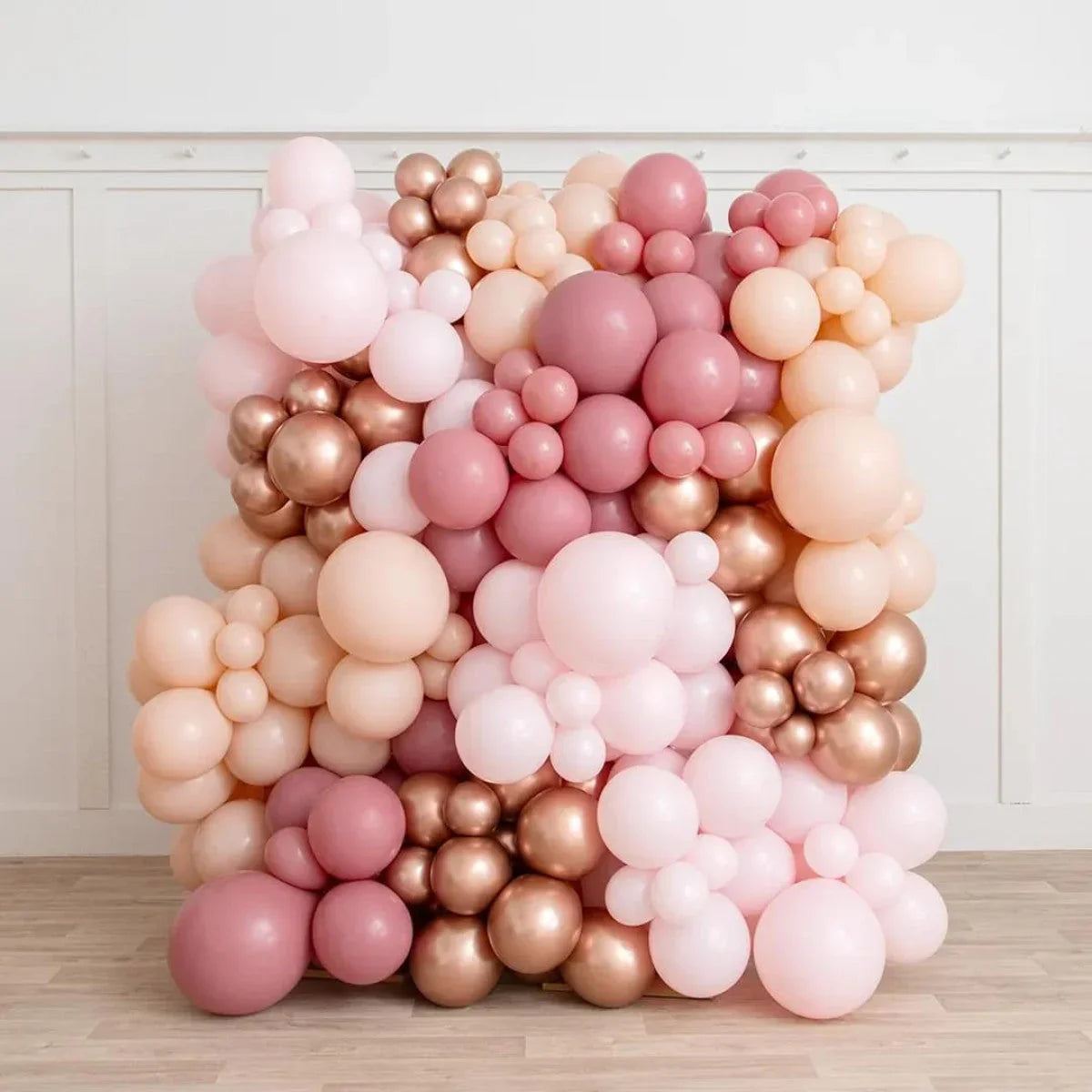 Rose gold, pink, and peach balloon wall decoration set against white paneled wall