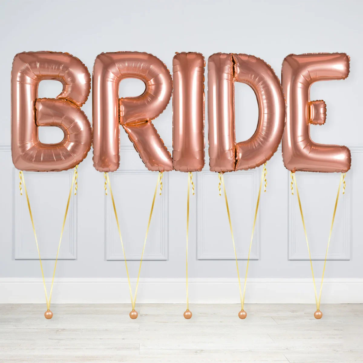 Rose gold foil balloons spelling BRIDE, tied with gold ribbons on light floor