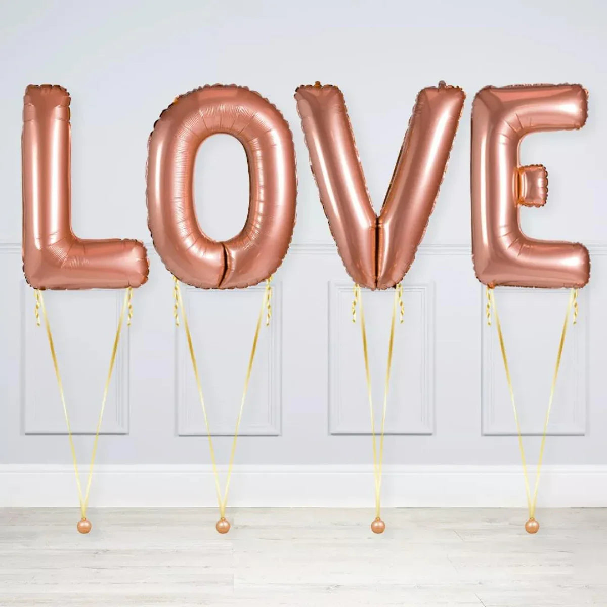 Rose gold foil balloons spelling LOVE with yellow strings in a light room on wooden floor