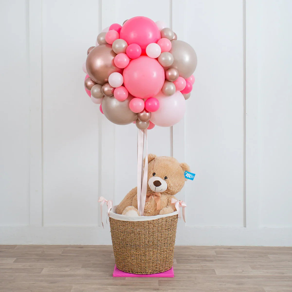 Teddy bear in wicker basket under rose gold and pink balloon arrangement indoor