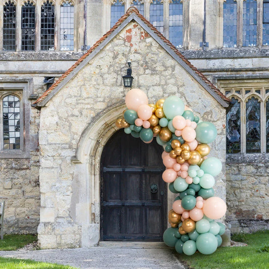 Sage green, blush, and gold balloon arch decoration on a stone church doorway